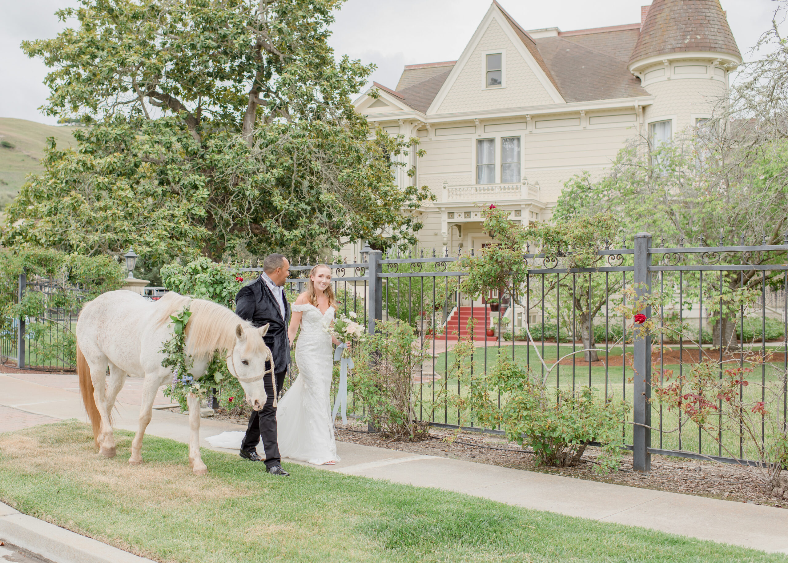 groom and bride walking in front of chateau with white horse