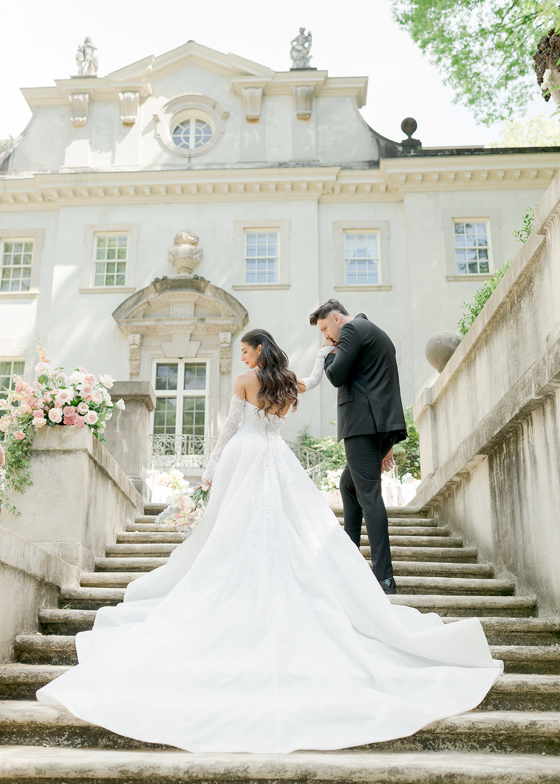 bride and groom walking up stairs while he kisses her hand